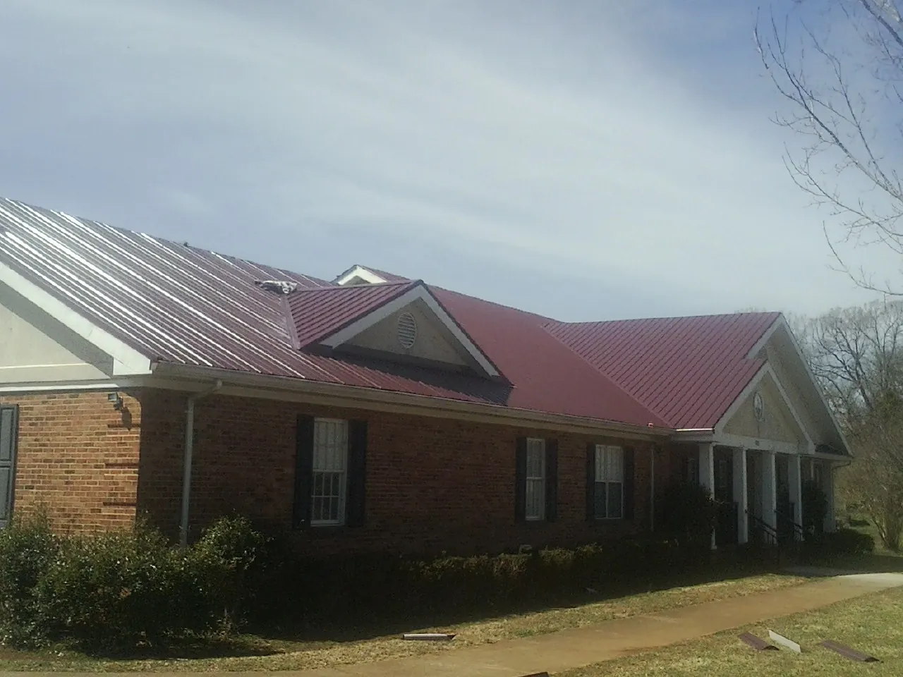 Red metal roof with gabled entries on a long brick building, from a Hail Damage Roof Repair job in Colville