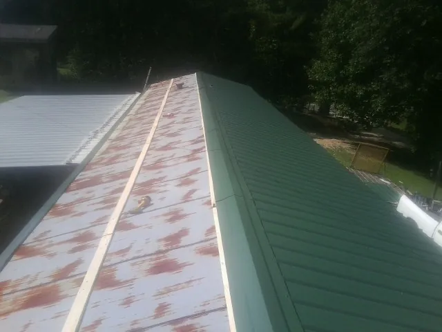 Old rusted panels beside newly installed green metal roofing — Wind Damage Roof Repair by Roofing Brothers in Colville