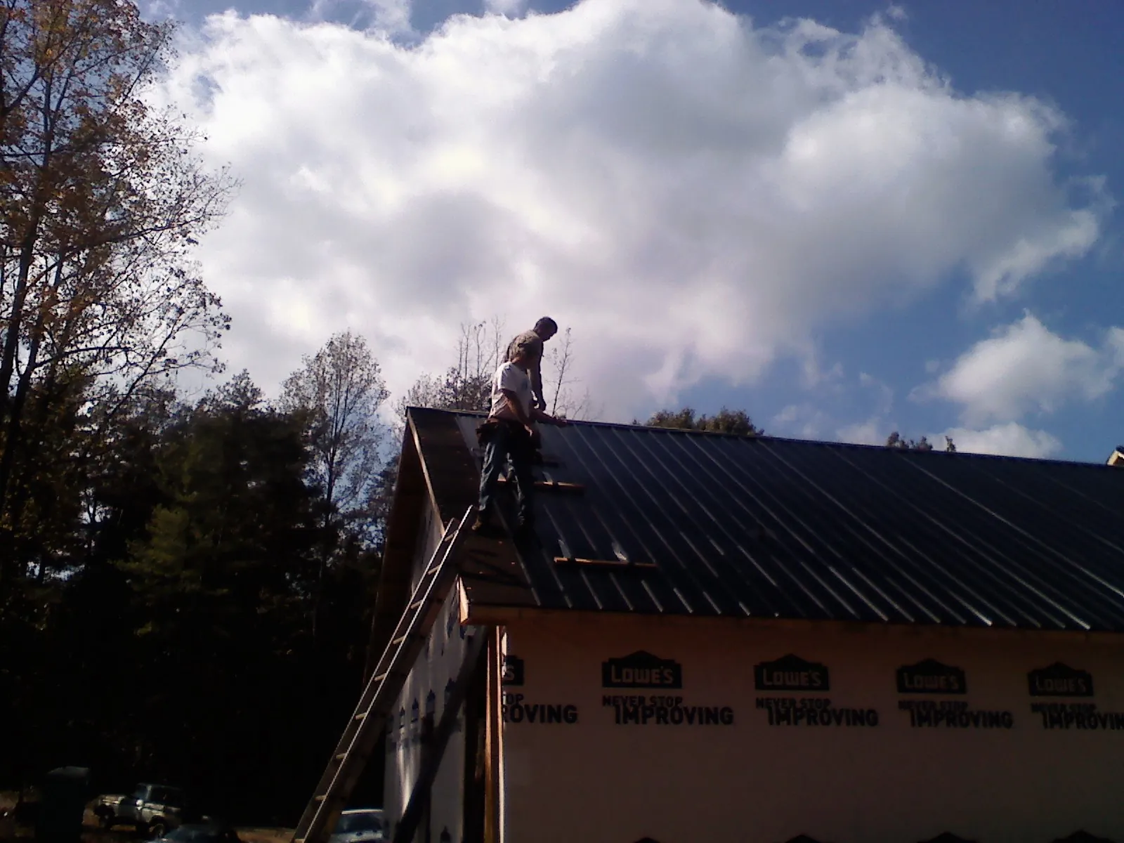 Roofer fastening dark metal panels high against a cloudy sky, from a Roof Inspection job in Colville