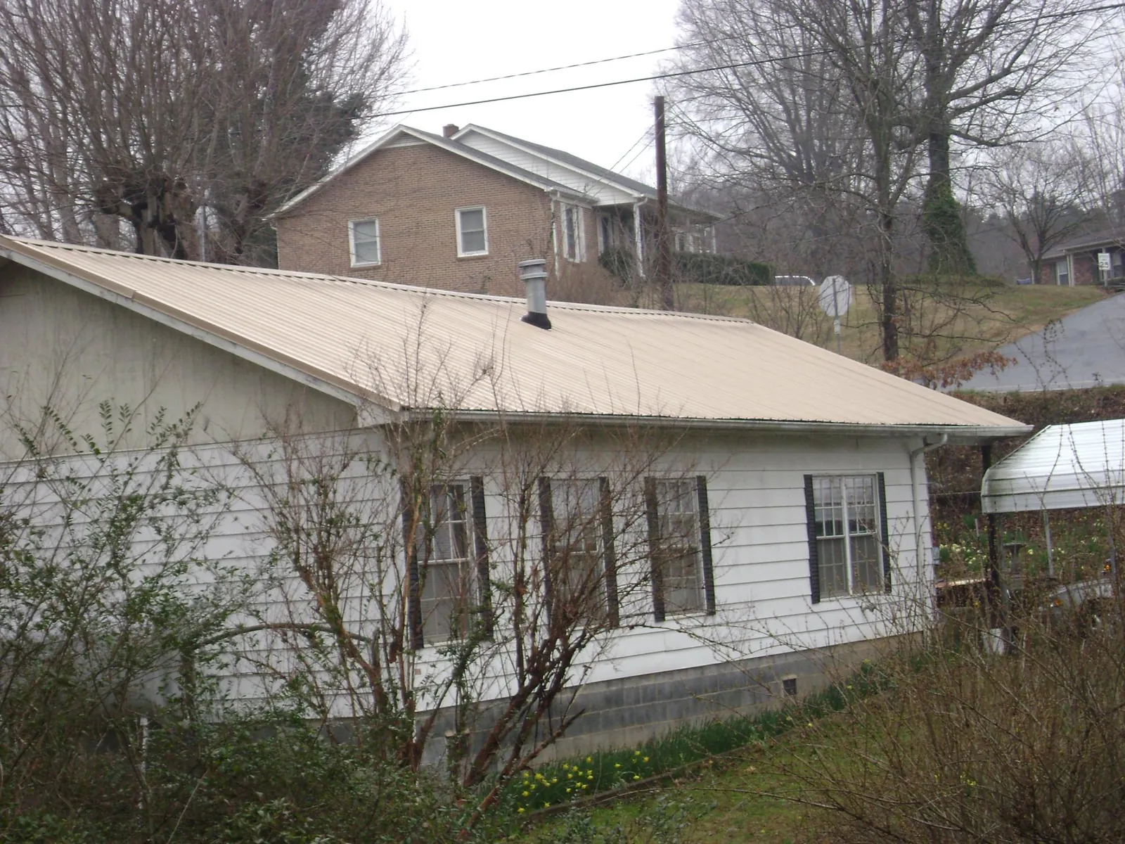 Tan metal roof on a white sided house set into a hillside — Commercial Roofing by Roofing Brothers in Colville